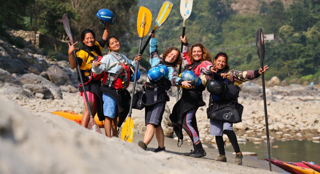 Kvinnliga forsguider i Nepal poserar med sina paddlar på en strand